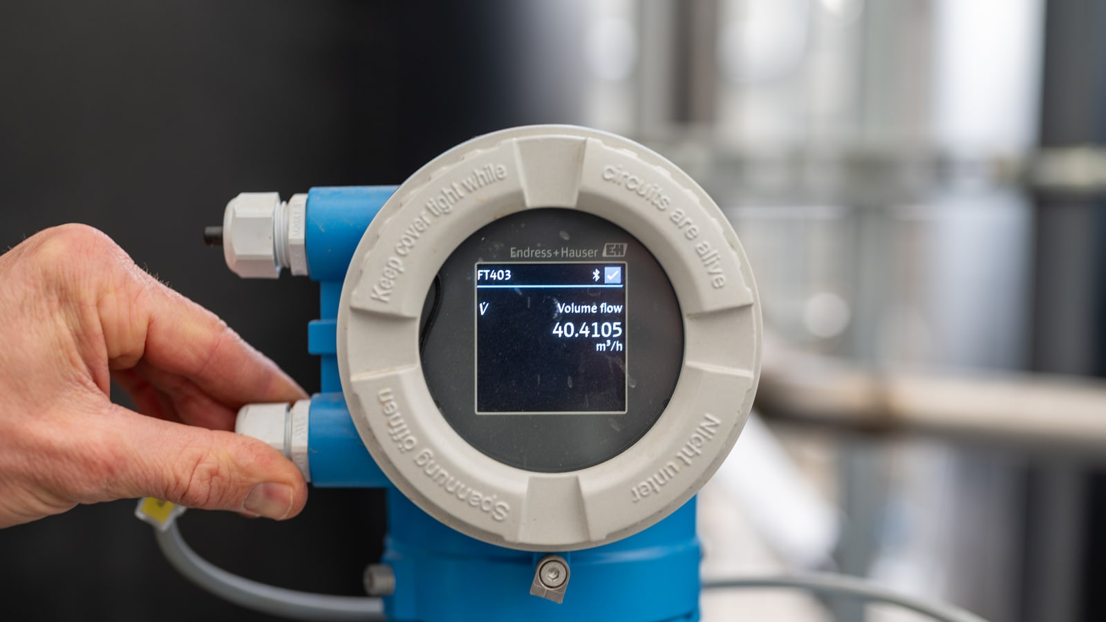 A flow meter transmitter on a process line, its display reading a volume flow in cubic metres an hour
