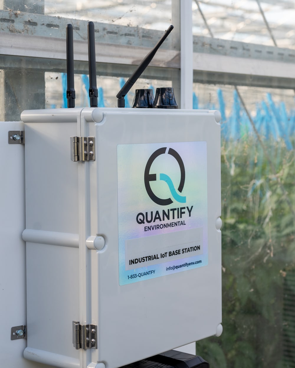 A Quantify base station enclosure with three antennas, mounted on a post in a greenhouse