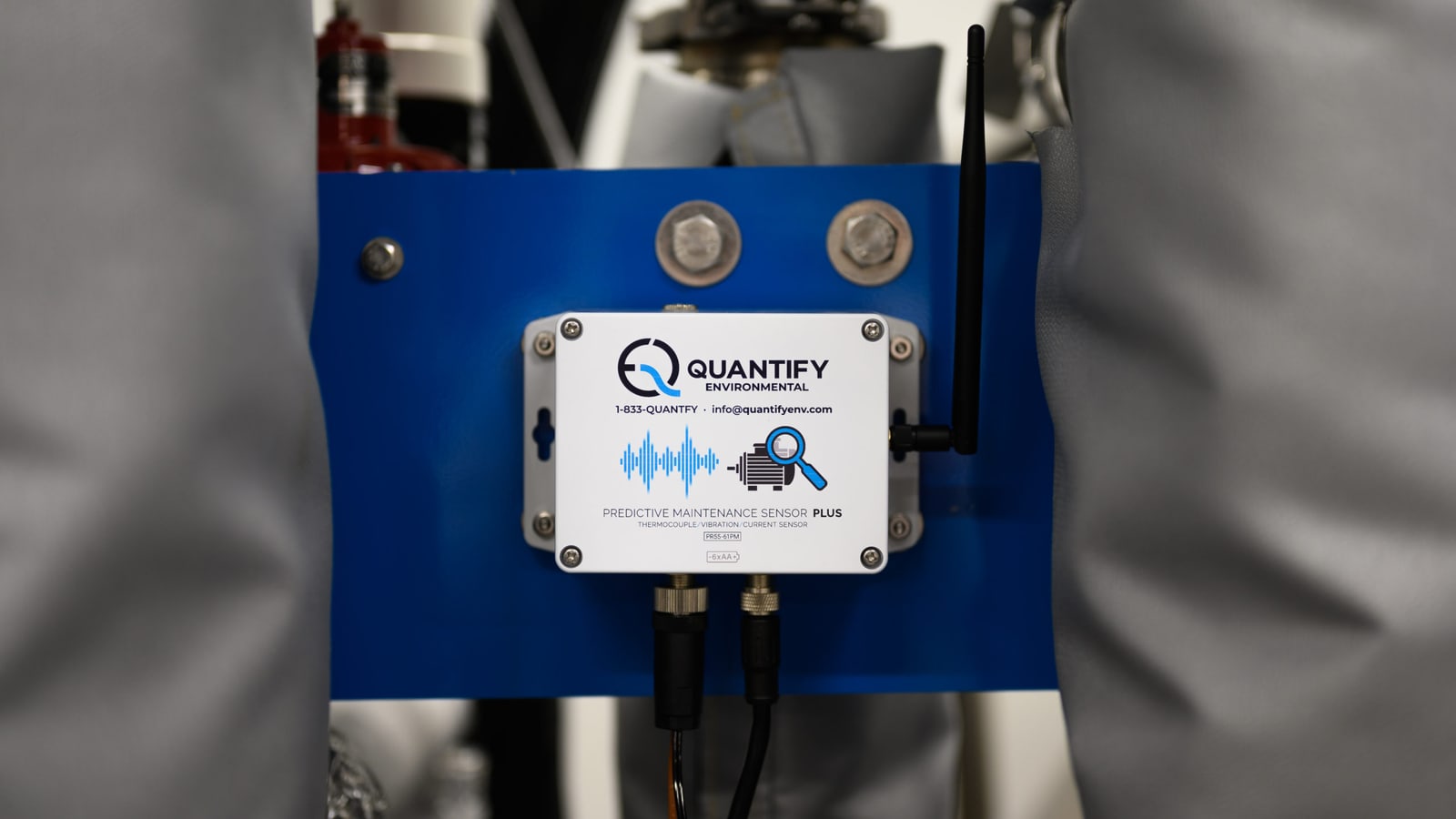 A Quantify predictive maintenance sensor bolted to the blue frame of a plant machine, its antenna raised