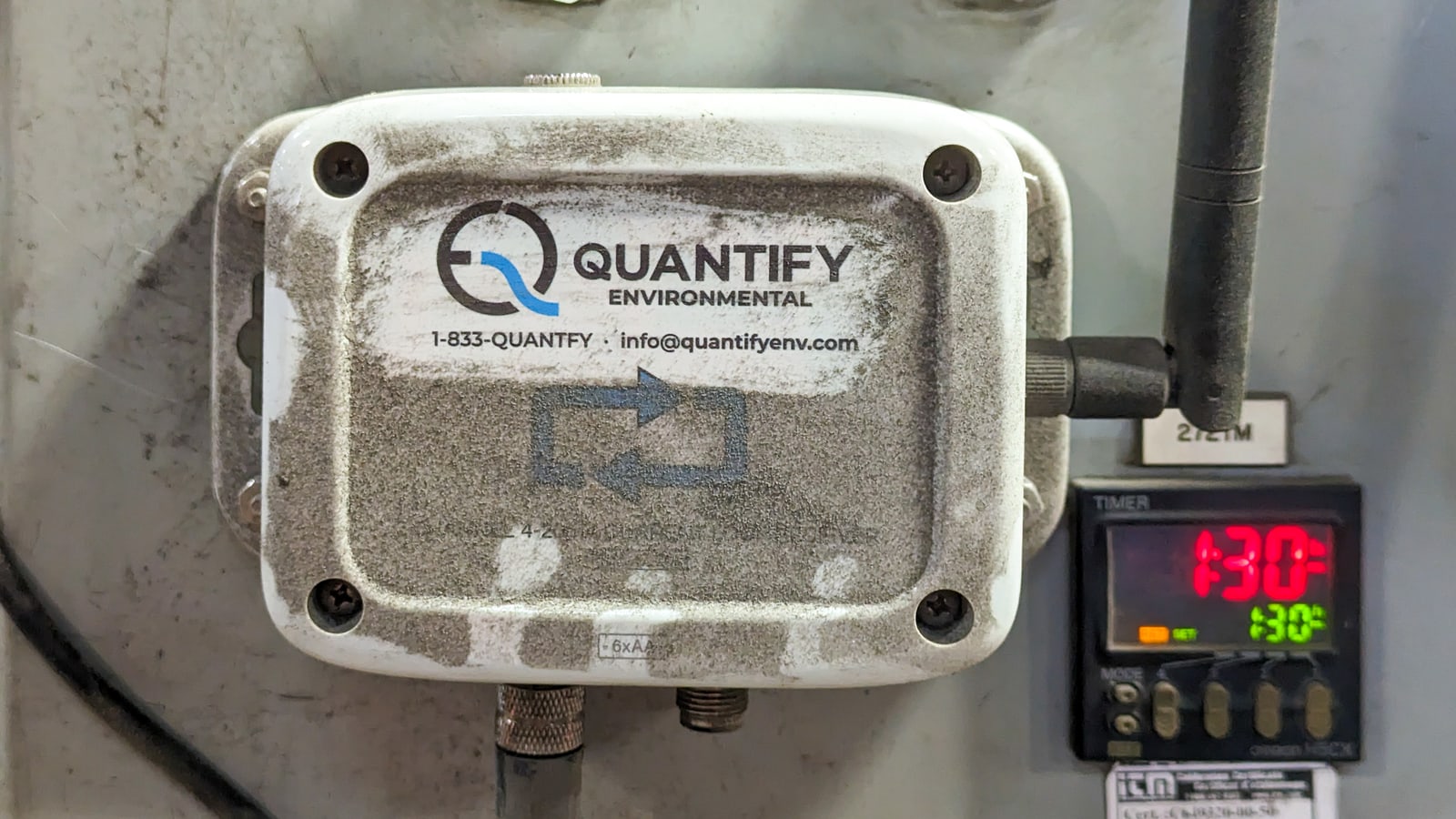A Quantify sensor enclosure caked in plant dust after months in service, beside a process temperature controller